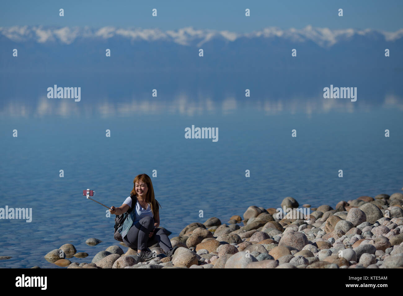 Ein weibliches Modell am Südufer von Issyk-Kol in Kirgisistan, im Hintergrund spiegeln sich die Berge des Nordufers. Stockfoto