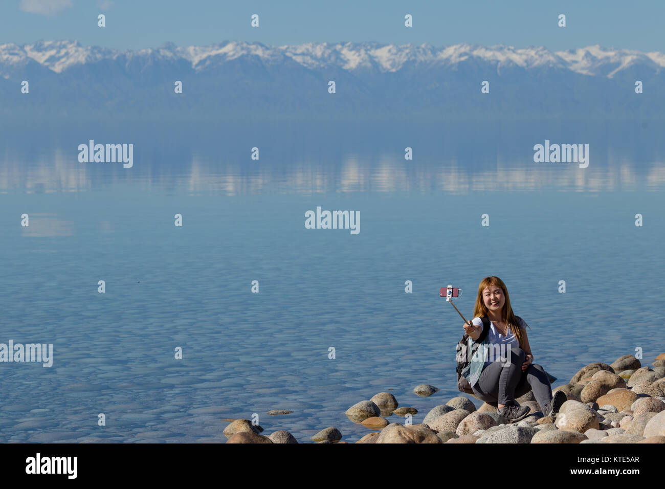 Ein weibliches Modell am Südufer von Issyk-Kol in Kirgisistan, im Hintergrund spiegeln sich die Berge des Nordufers. Stockfoto
