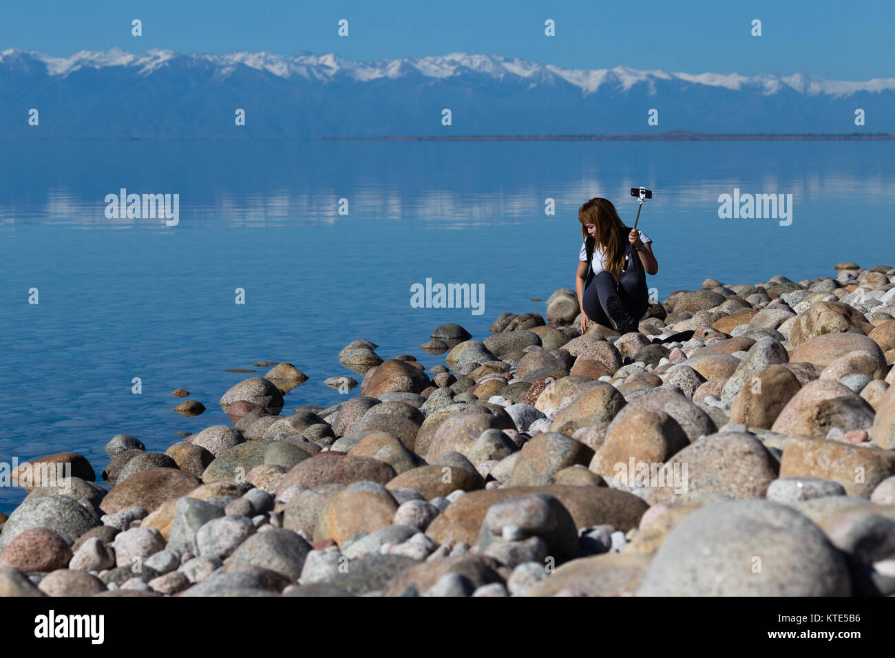 Ein weibliches Modell am Südufer von Issyk-Kol in Kirgisistan, im Hintergrund spiegeln sich die Berge des Nordufers. Stockfoto