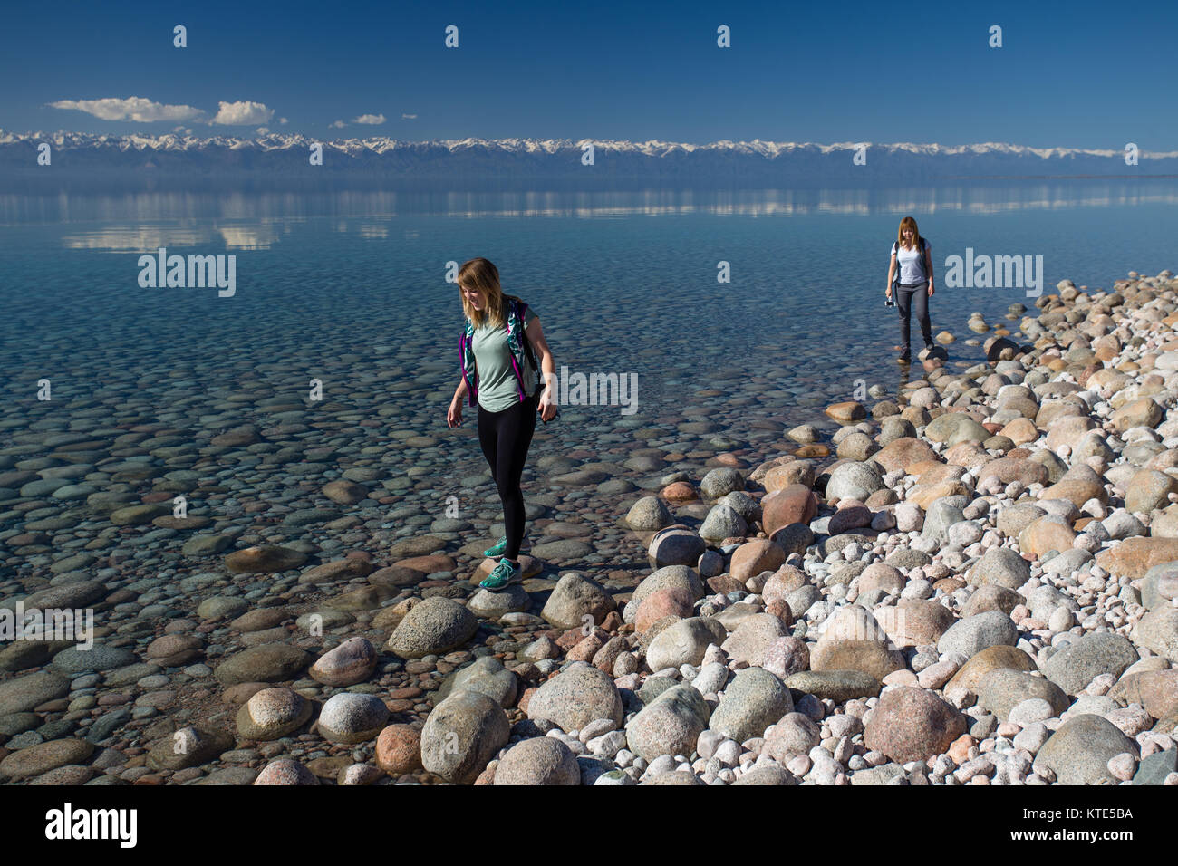 Zwei weibliche Touristen aus der Mitte der 20er Jahre, die am Südufer des Issyk-Kol-Sees in Kirgisistan entlang wandern. Stockfoto