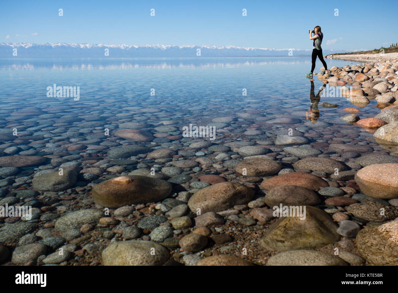 Ein weibliches Modell am Südufer von Issyk-Kol in Kirgisistan, im Hintergrund spiegeln sich die Berge des Nordufers. Stockfoto