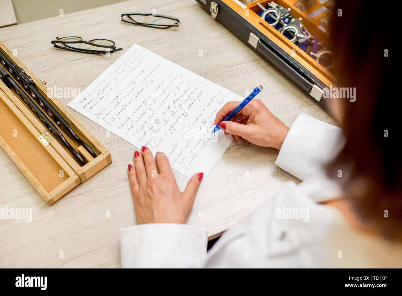 Senior augenarzt Schreiben von wissenschaftlichen Arbeiten auf dem Tisch mit Brillen und verschiedene Objektive Stockfoto