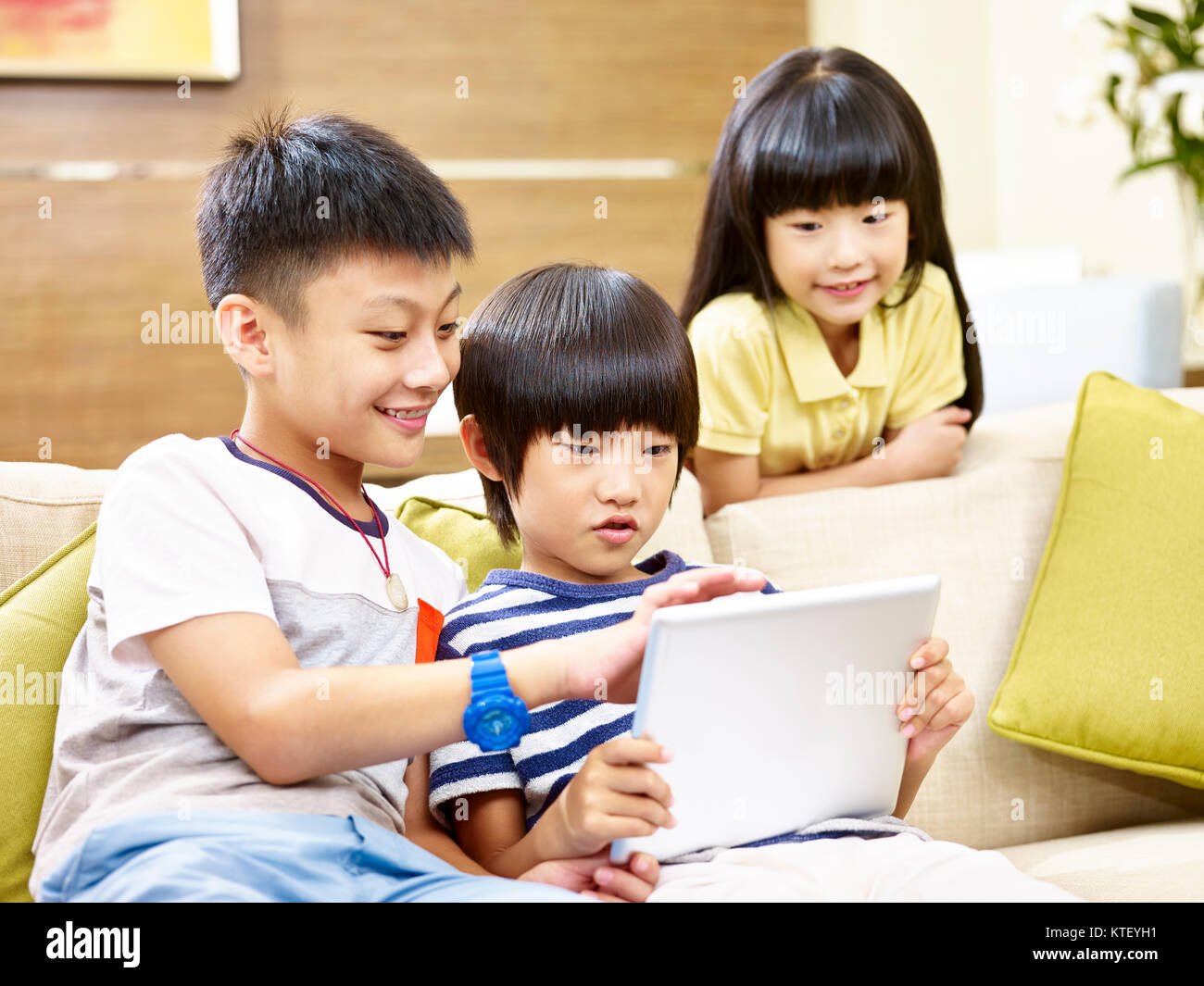 Drei asiatische Kinder zwei kleiner Junge und ein kleines Mädchen saß auf der Couch zu Hause spielen video game mit digitalen Tablet, konzentrieren sich auf die wenig boyin der Stockfoto