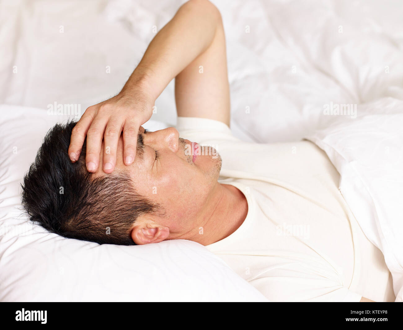 Asiatischer Mann lag auf dem Rücken im Bett die Hand auf die Stirn. Stockfoto