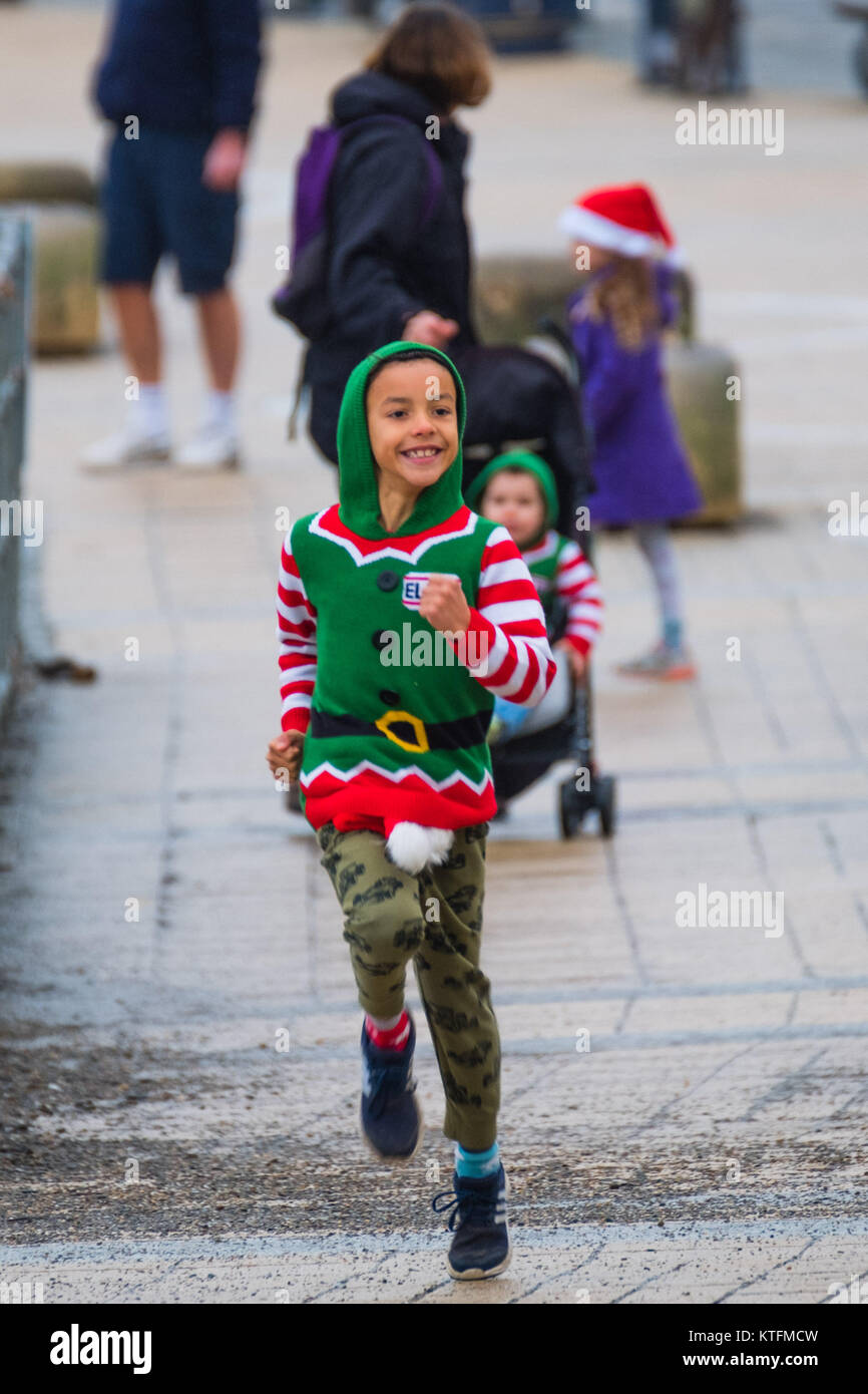 Aberystwyth Wales UK, Heiligabend, Sonntag, den 24. Dezember 2017 Großbritannien Wetter: Ein kleiner Junge gekleidet wie Santa's Helper glücklich auf der Strandpromenade in Aberystwyth Wales auf einen bemerkenswert mild, aber bewölkt und feucht, Heiligabend. Temperaturen über viel ofg Großbritannien in der 10-12°C reichen heute sein wird, bevor Sie wesentlich kälter und windiger, später in der Woche Foto © Keith Morris Credit: Keith Morris/Alamy leben Nachrichten Stockfoto