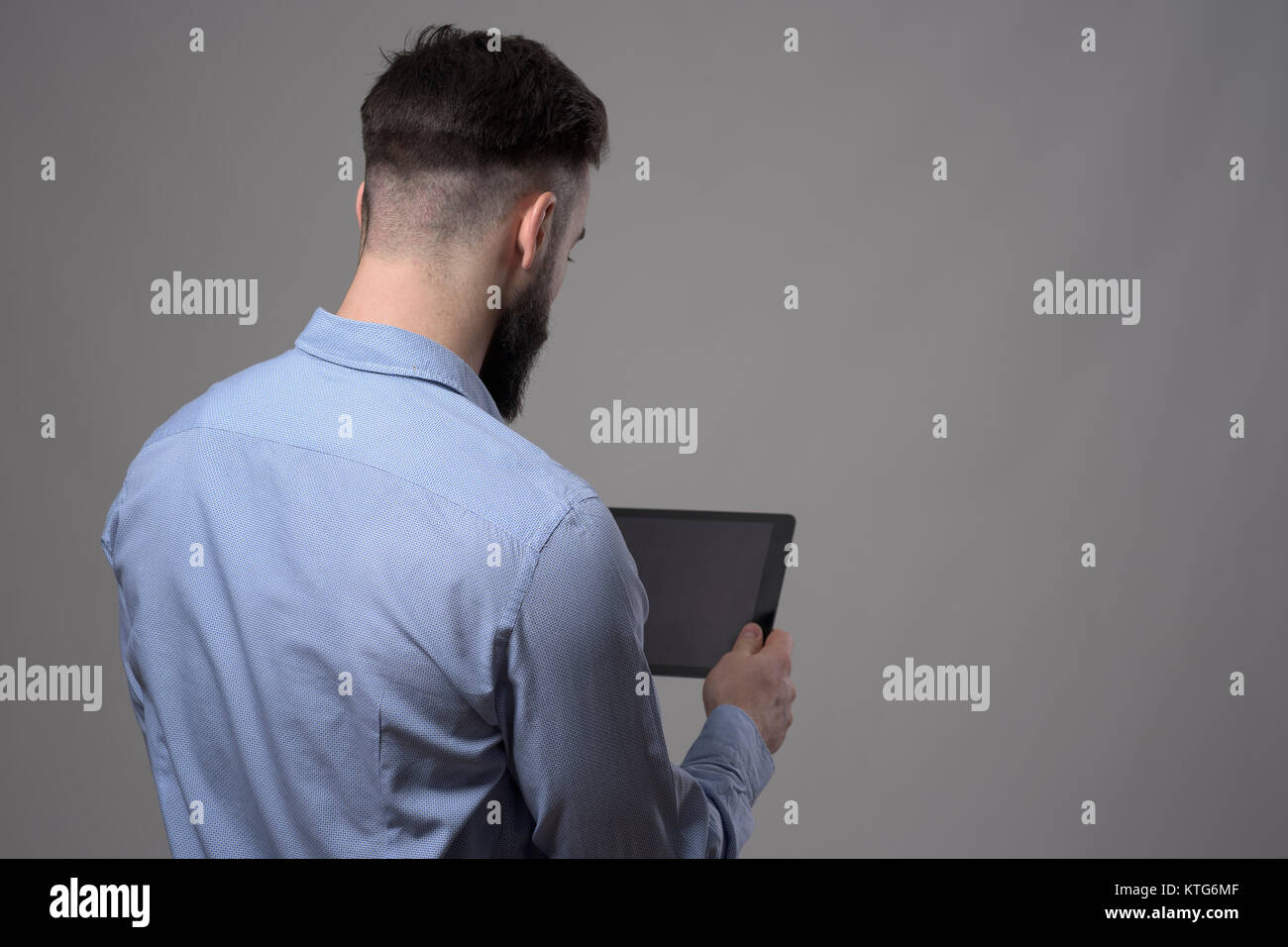 Blick über die Schulter junger Geschäftsmann Holding und lesen leeres Tablet Computer über Grau studio Hintergrund mit Copyspace Stockfoto
