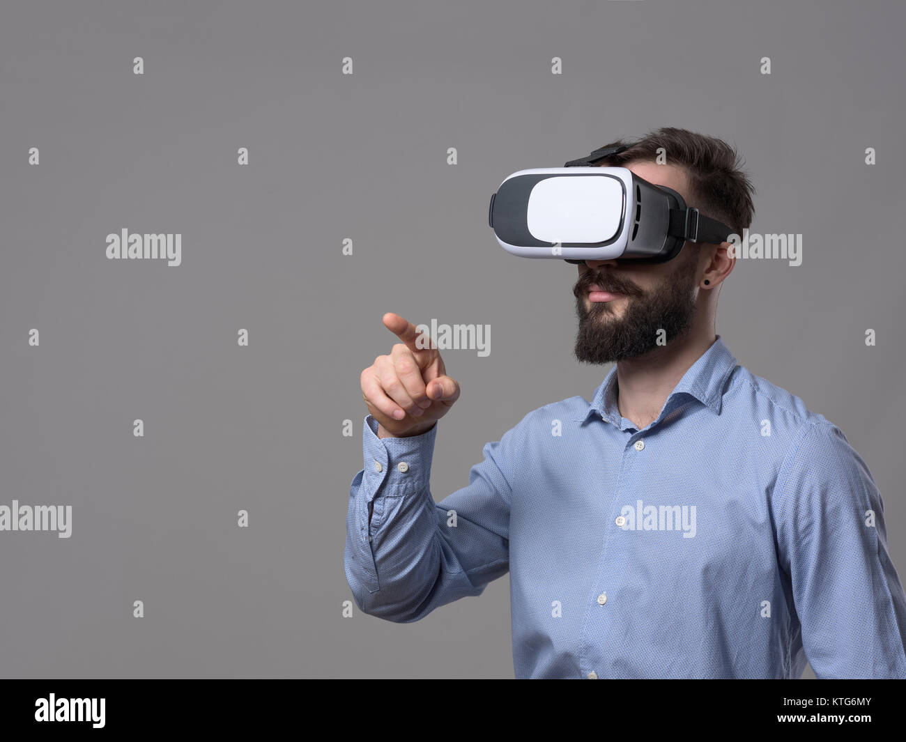 Business Mann mit Virtual reality Brillen punkte Finger und Interagieren mit Augmented Reality Touchscreen mit Copyspace über grauen Hintergrund. Stockfoto