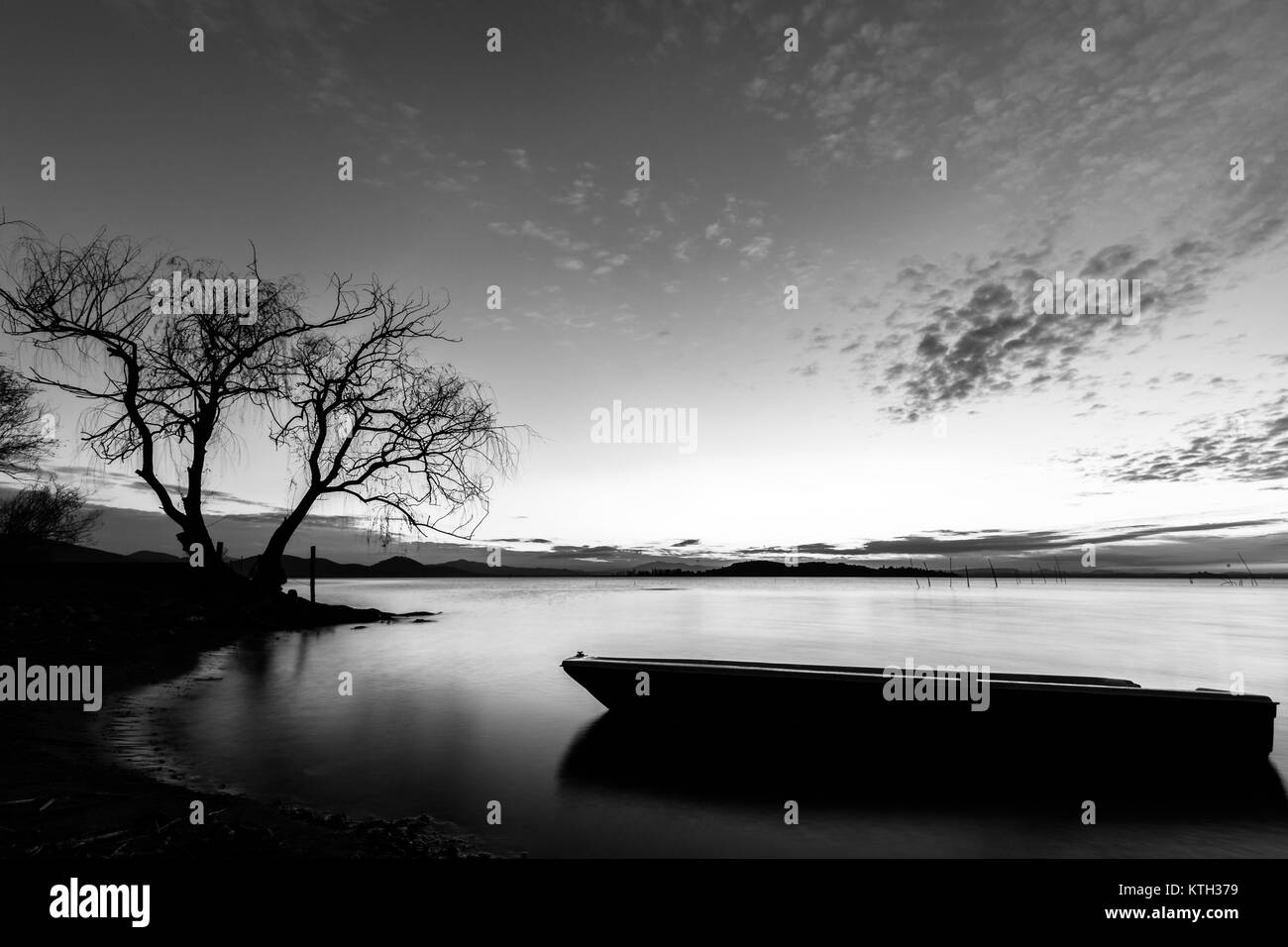 Schönen Blick auf den Trasimenischen See (Umbrien) in der Dämmerung, mit einem kleinen Boot Silhouette in den Vordergrund, perfekt noch Wasser und ein Baum im Hintergrund Stockfoto