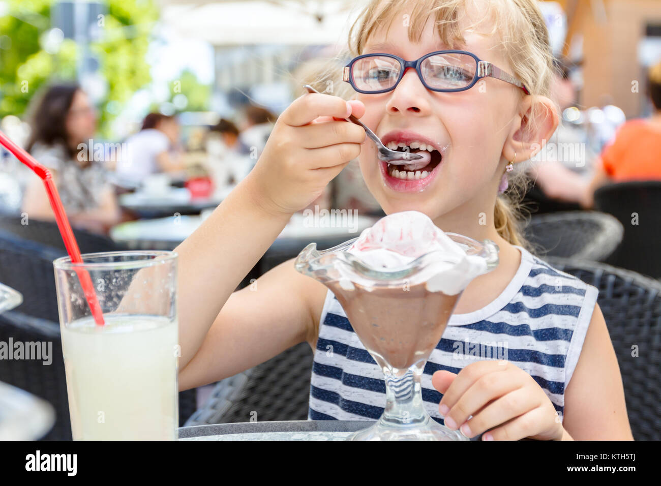 Kleine süße Mädchen mit Brille und sorglos Gesichtsausdruck ist Eis essen am Tisch in der Konditorei im Sommer. Stockfoto