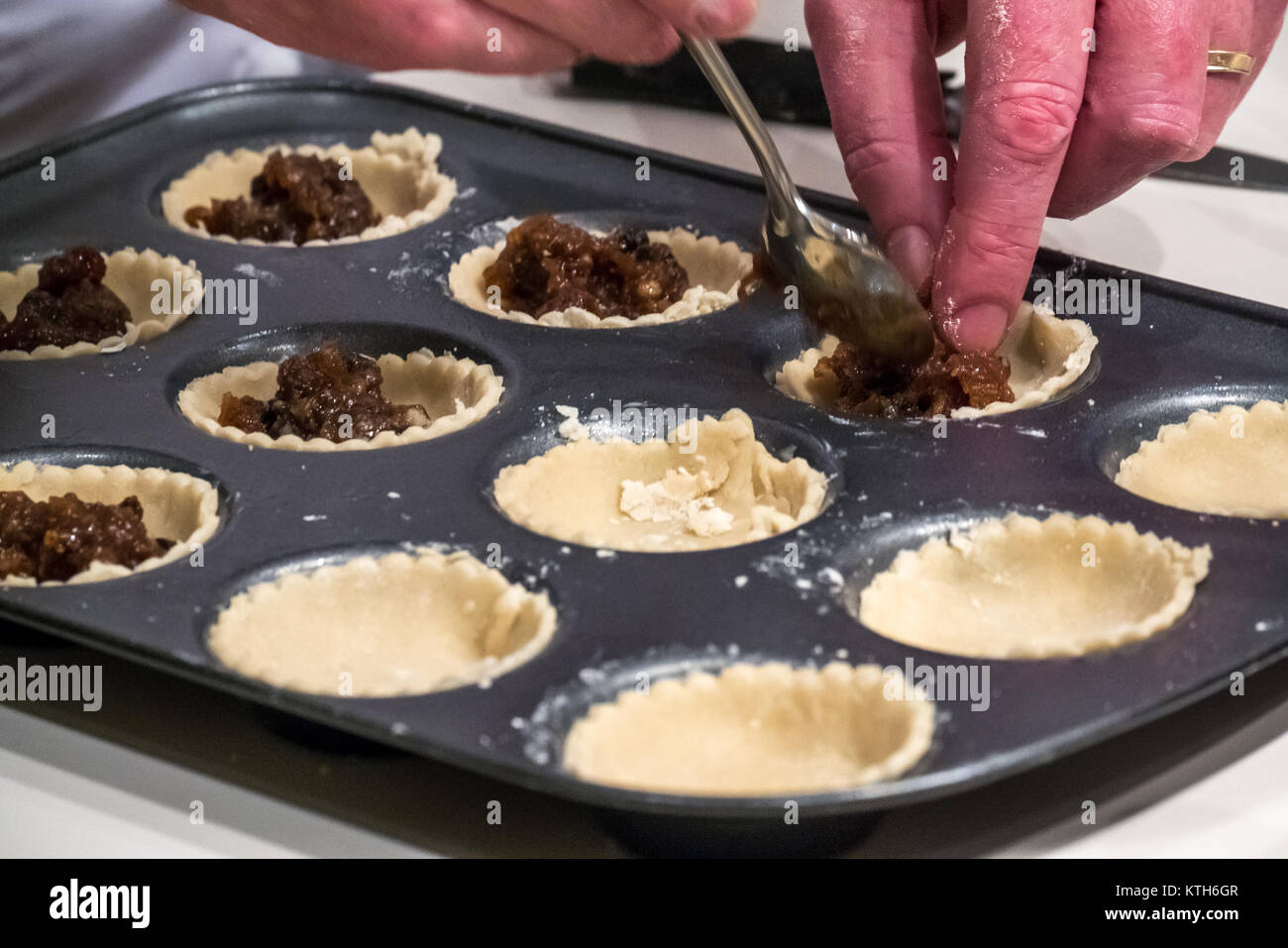 Nahaufnahme der Hände des Menschen Füllung Mince Pie Fällen mit Hackfleisch bereit zum Backen auf einer weißen Küchentheke Stockfoto