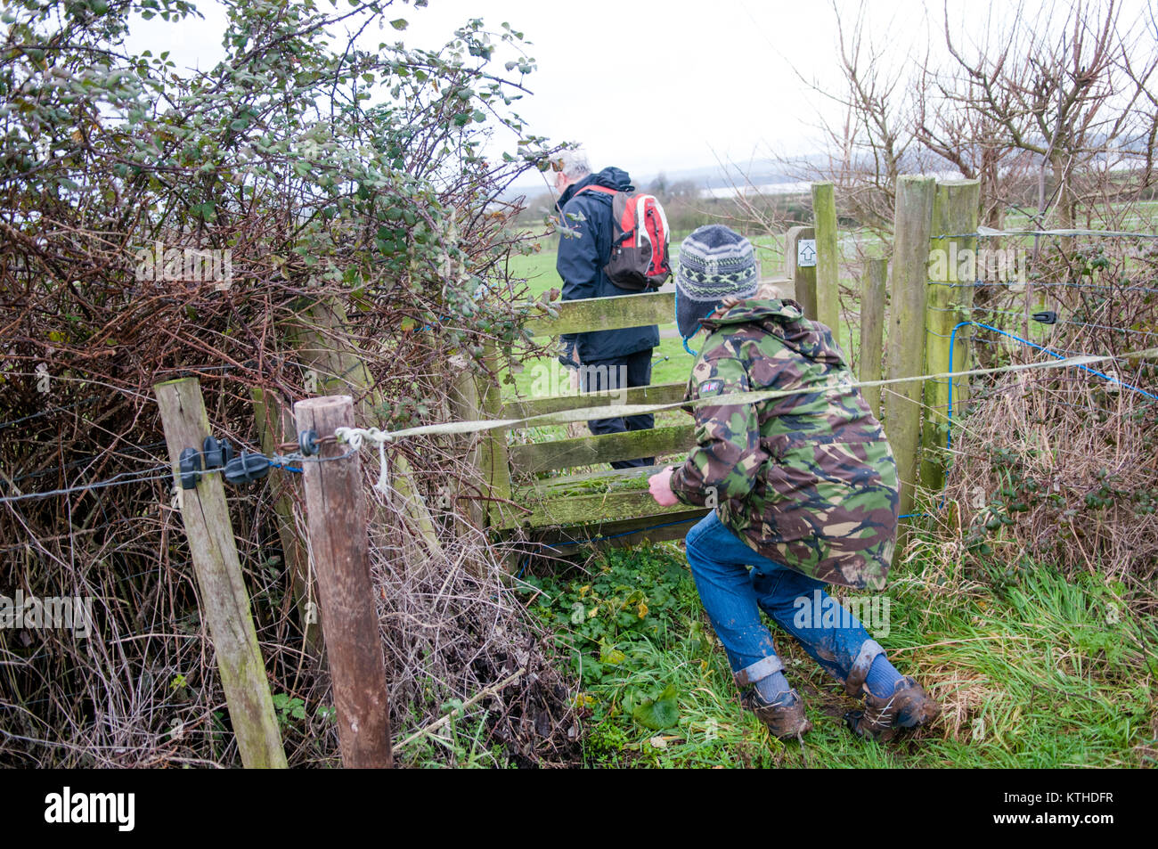Zwei Wanderer versuchen, hinter einem elektrischen Zaun vor einem öffentlichen Fußweg und Stil in Felder in der Landschaft im Winter zu erhalten Stockfoto