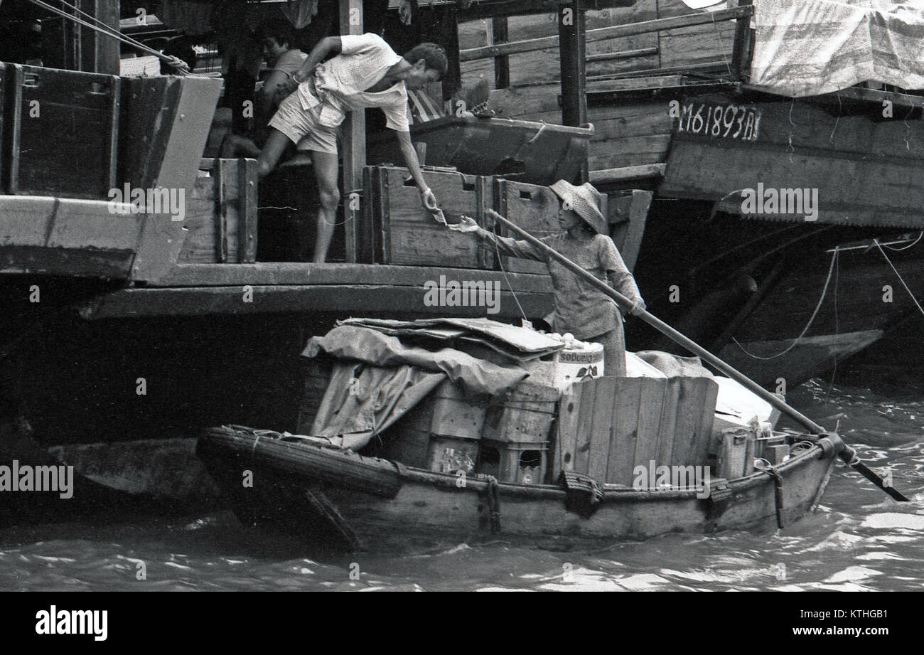 Hafen Aberdeen, HONG KONG, Februar 1981: Frau im Sampan erhält das Geld für ihre Gemüse aus Mann auf Junk, Februar 1981 im Hafen Aberdeen, Hong Kong. Dieser Hafen war die Heimat der Flüchtlinge im kommunistischen China. Stockfoto