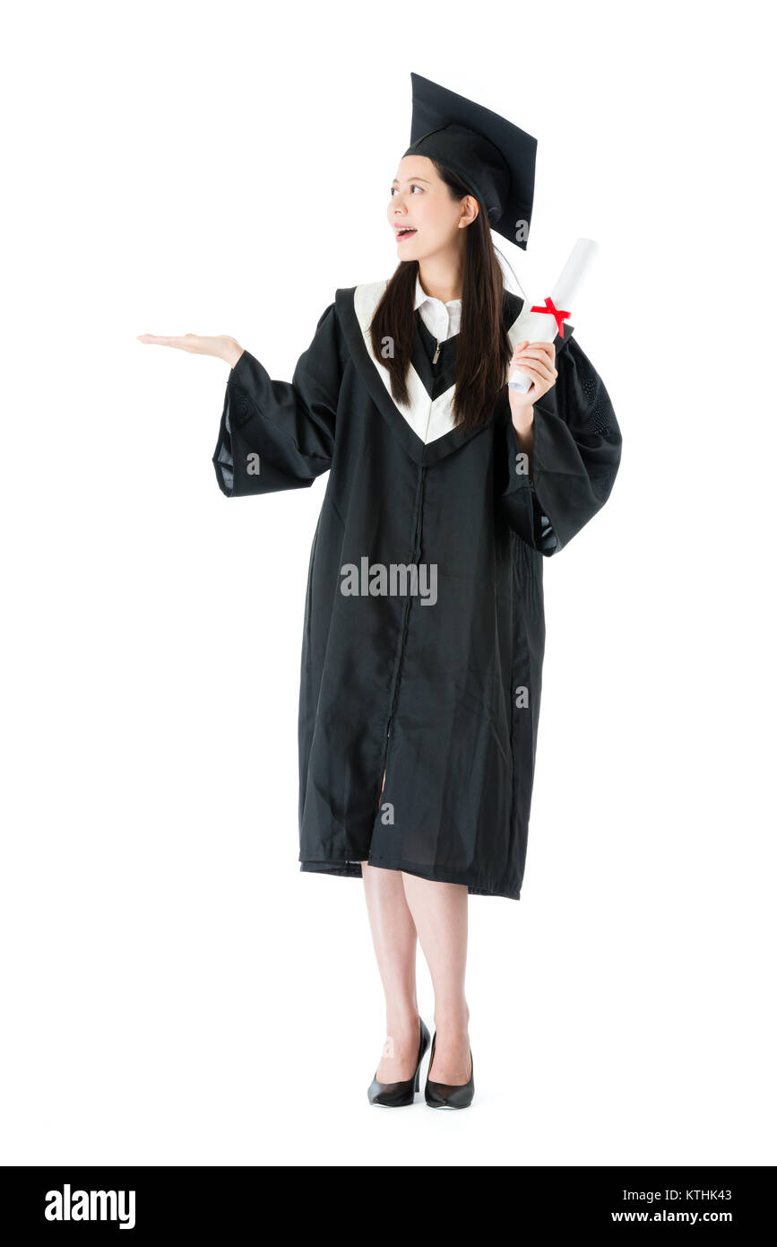 Lächelnd elegante Frau Student trägt die Graduierung Kleidung stehen auf weißen Hintergrund und Präsentation Geste leeren Bereich. Stockfoto