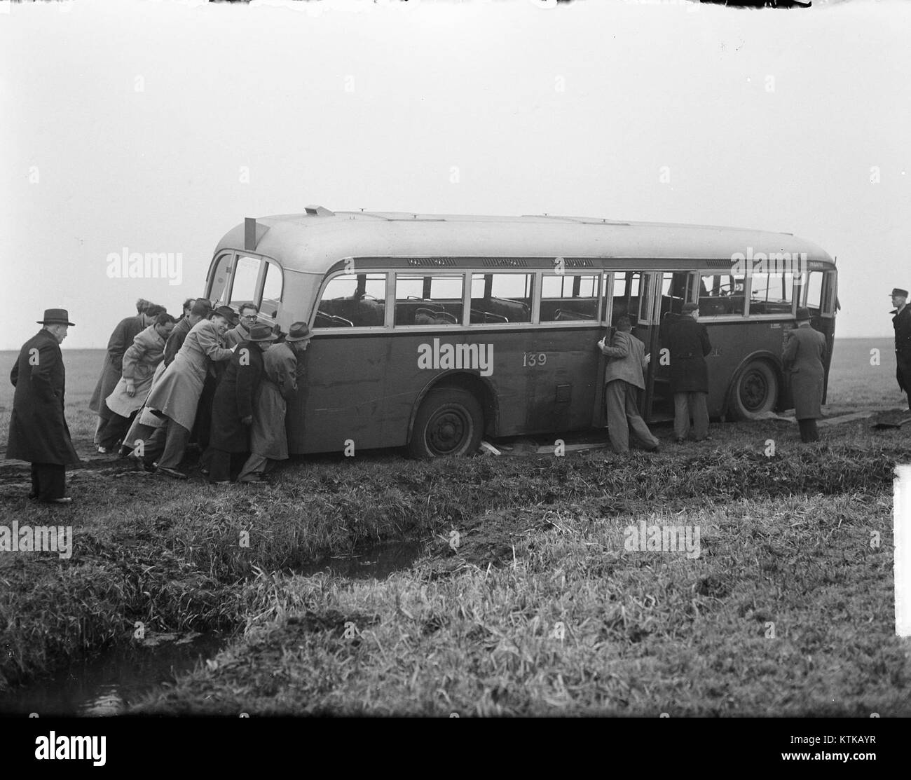 Dieses historische Foto zeigt Passagiere, die einen Bus schieben. Das Bild ist eine Darstellung eines geschäftigen Moments, möglicherweise während eines Verkehrsproblems oder in einer überfüllten Umgebung, die das tägliche Leben im Europa des frühen 20. Jahrhunderts einfängt. Stockfoto Dieses historische Foto zeigt Passagiere, die einen Bus schieben. Das Bild ist eine Darstellung eines geschäftigen Moments, möglicherweise während eines Verkehrsproblems oder in einer überfüllten Umgebung, die das tägliche Leben im Europa des frühen 20. Jahrhunderts einfängt. Stockfoto