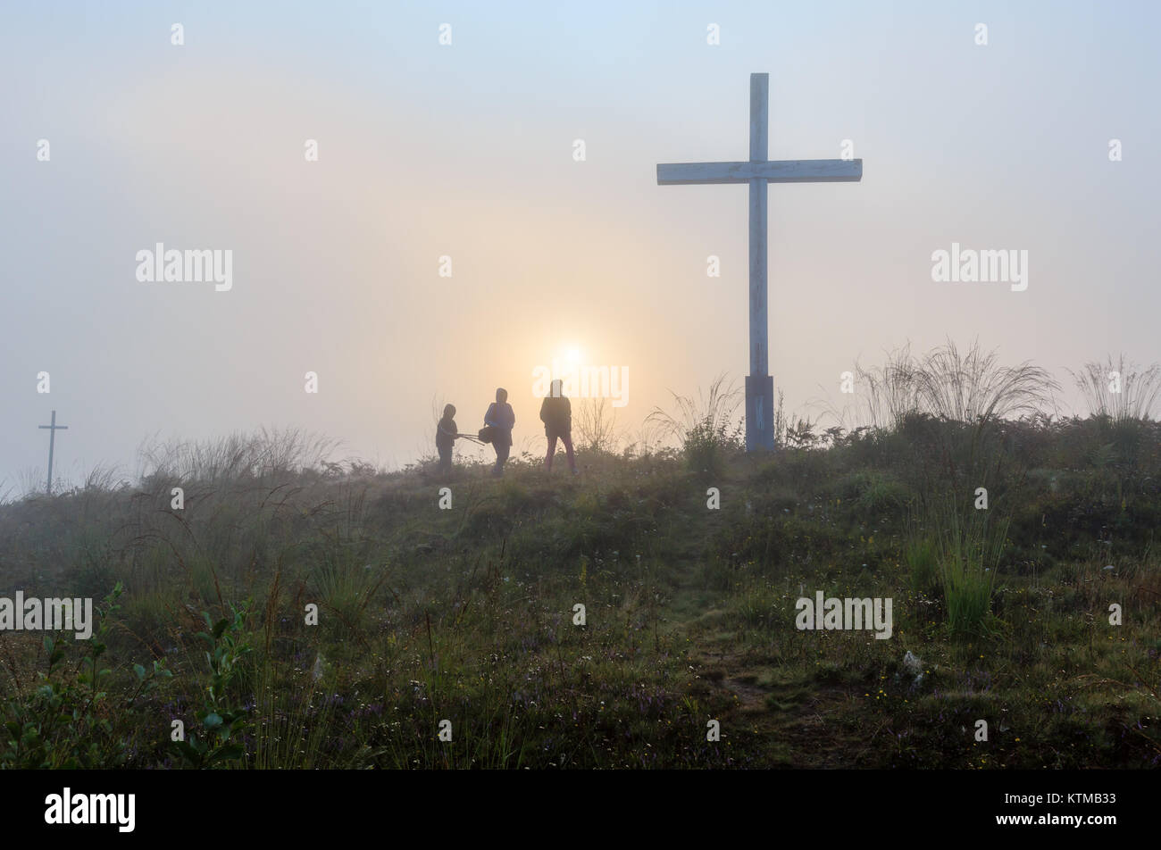 Misty Morning Sunrise Tau auf Wild Mountain grasbewachsenen Hügel mit religiösen Kreuze und Familie zu Fuß durch pass auf sunshine Hintergrund. Stockfoto