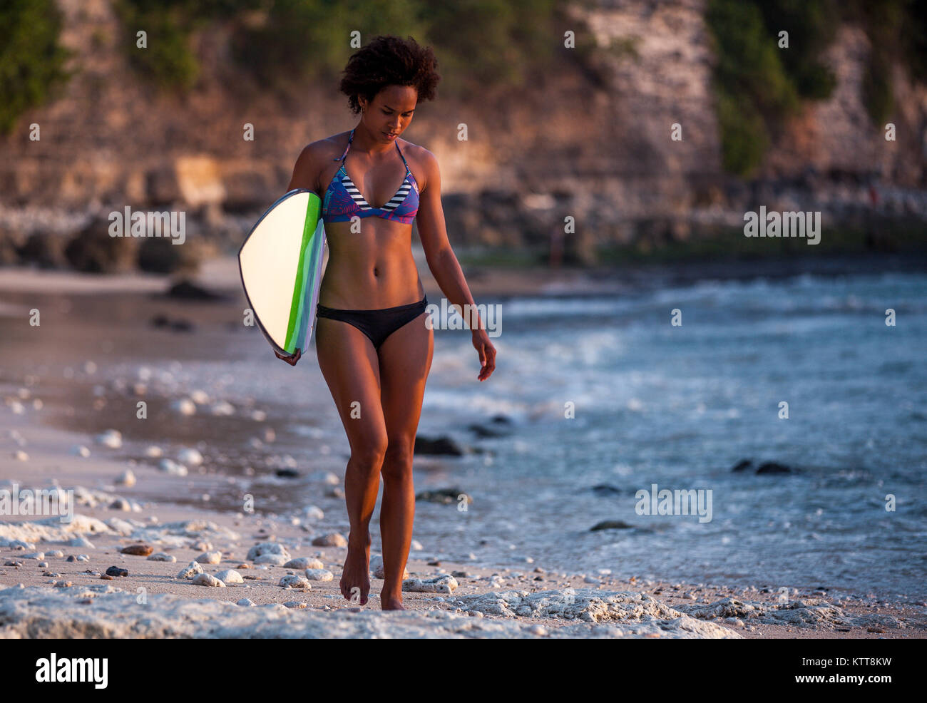 Surfer Girl mit Afro Frisur gehen mit Surfbrett auf dem Padang Padang Strand bei Sonnenuntergang auf Bali, Indonesien Stockfoto