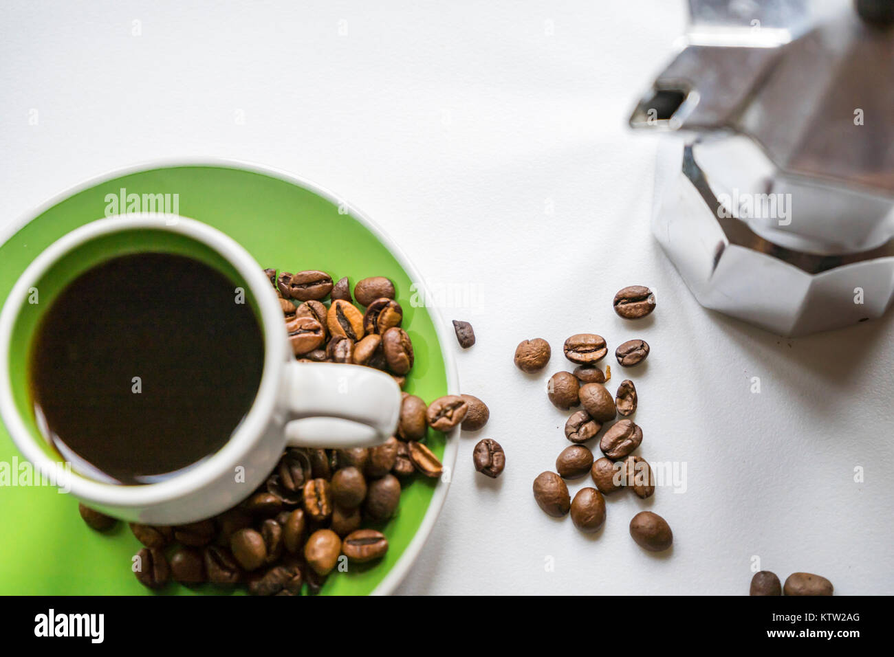 High-Angle Shot eines italienischen Moka Pot (Kaffeemaschine) und eine grüne Tasse Espresso mit Kaffeebohnen auf weißem Hintergrund Stockfoto