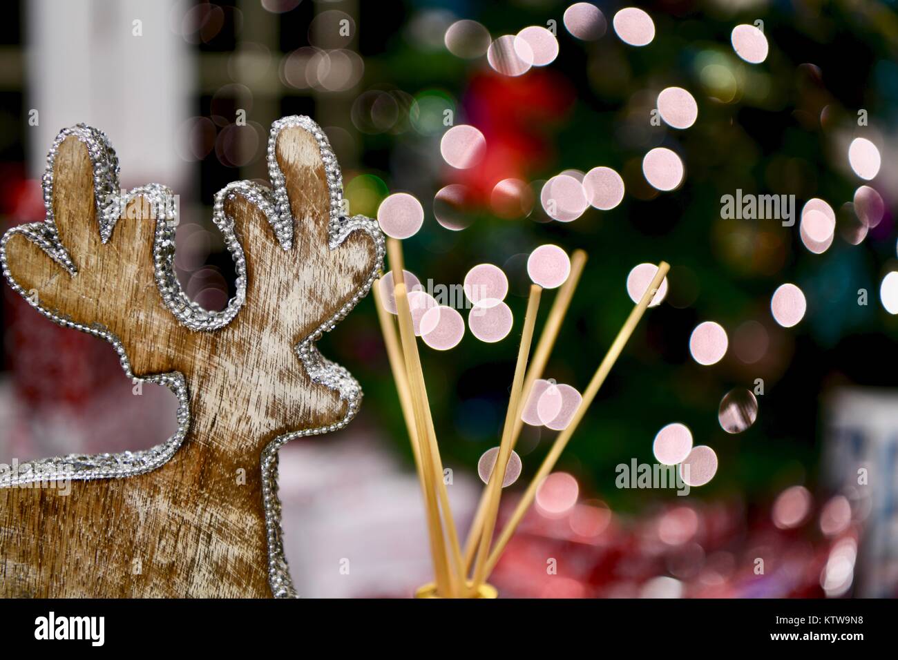 Holz- Rentier Weihnachten Dekor neben einem Reed Diffuser mit Weihnachtsbaum leuchtet im Hintergrund Stockfoto