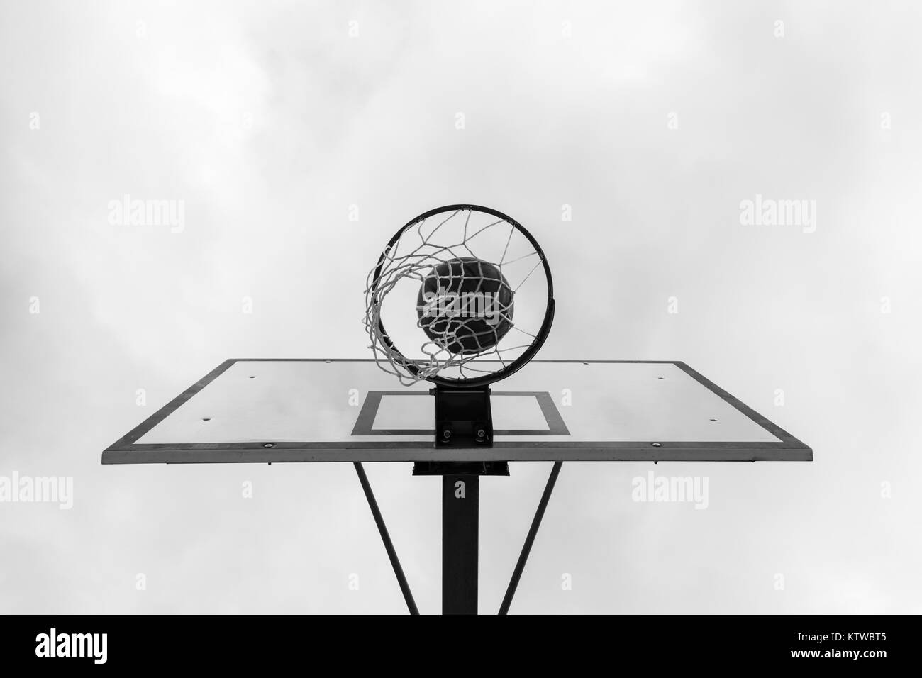 Schwarz-weiß Bild von einer Kugel im Inneren Basketballkorb, Korb gegen weißen Himmel. Outdoor Basketball Court. Stockfoto