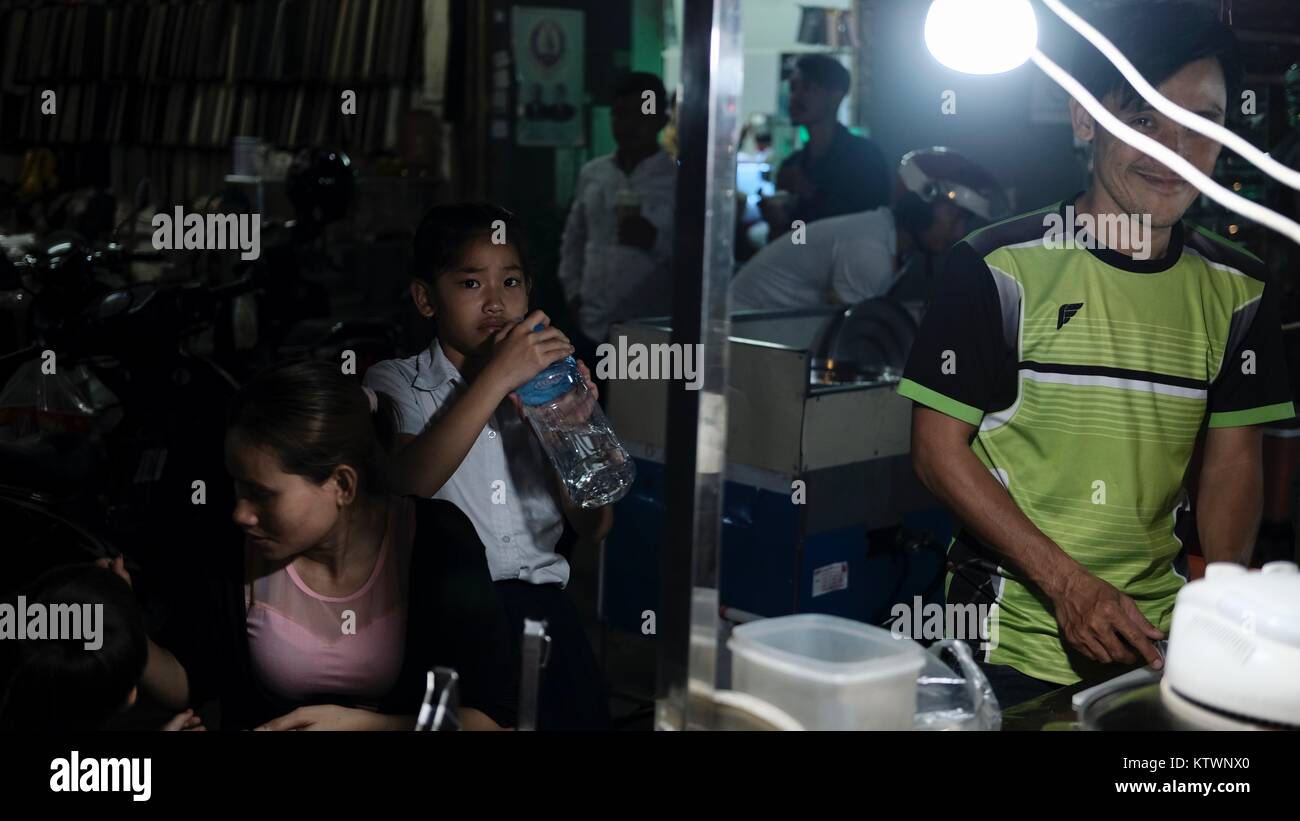 Junge trinkt Mineralwasser am Street Food Stand in der Oknha tep Phan Street 182 Phnom Penh Cambodia man in Green Shirt und bereitet Essen zu Stockfoto