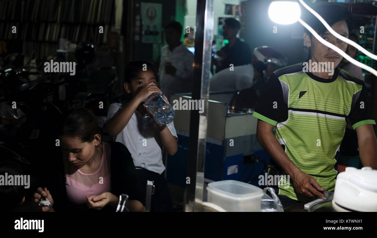 Junge trinkt Mineralwasser am Street Food Stand in der Oknha tep Phan Street 182 Phnom Penh Cambodia man in Green Shirt und bereitet Essen zu Stockfoto