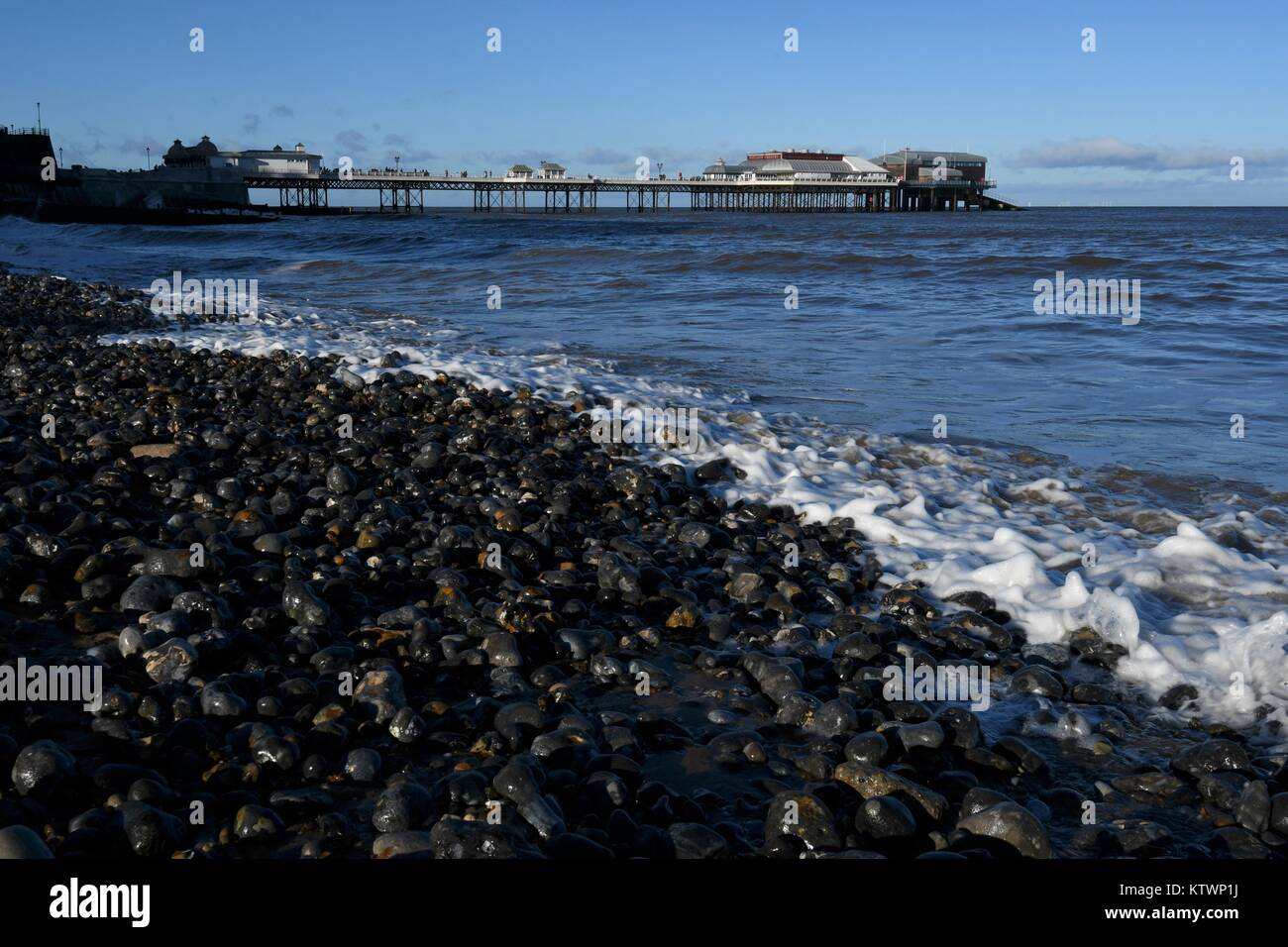 Cromer, Norfolk, Großbritannien. Wellen auf den Strand bei Cromer mit Cromer Pier im Hintergrund, ist das Zuhause der RNLI Cromer Rettungsboot Station Stockfoto