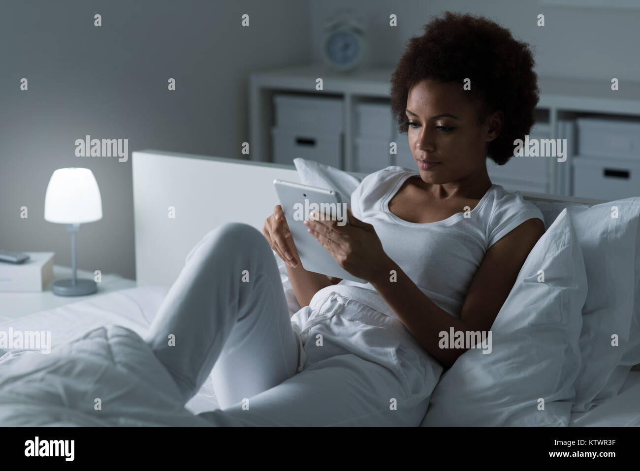 Junge afrikanische amerikanische Frau entspannt auf dem Bett, sie lächelt und Filme mit einem Touchscreen tablet, Freizeit und Lifestyle Konzept Stockfoto