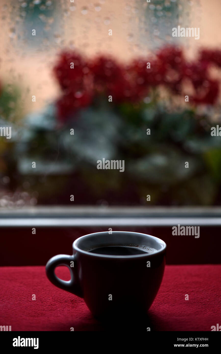 Heiße Tasse Kaffee vor Fenster Regentropfen Stockfoto