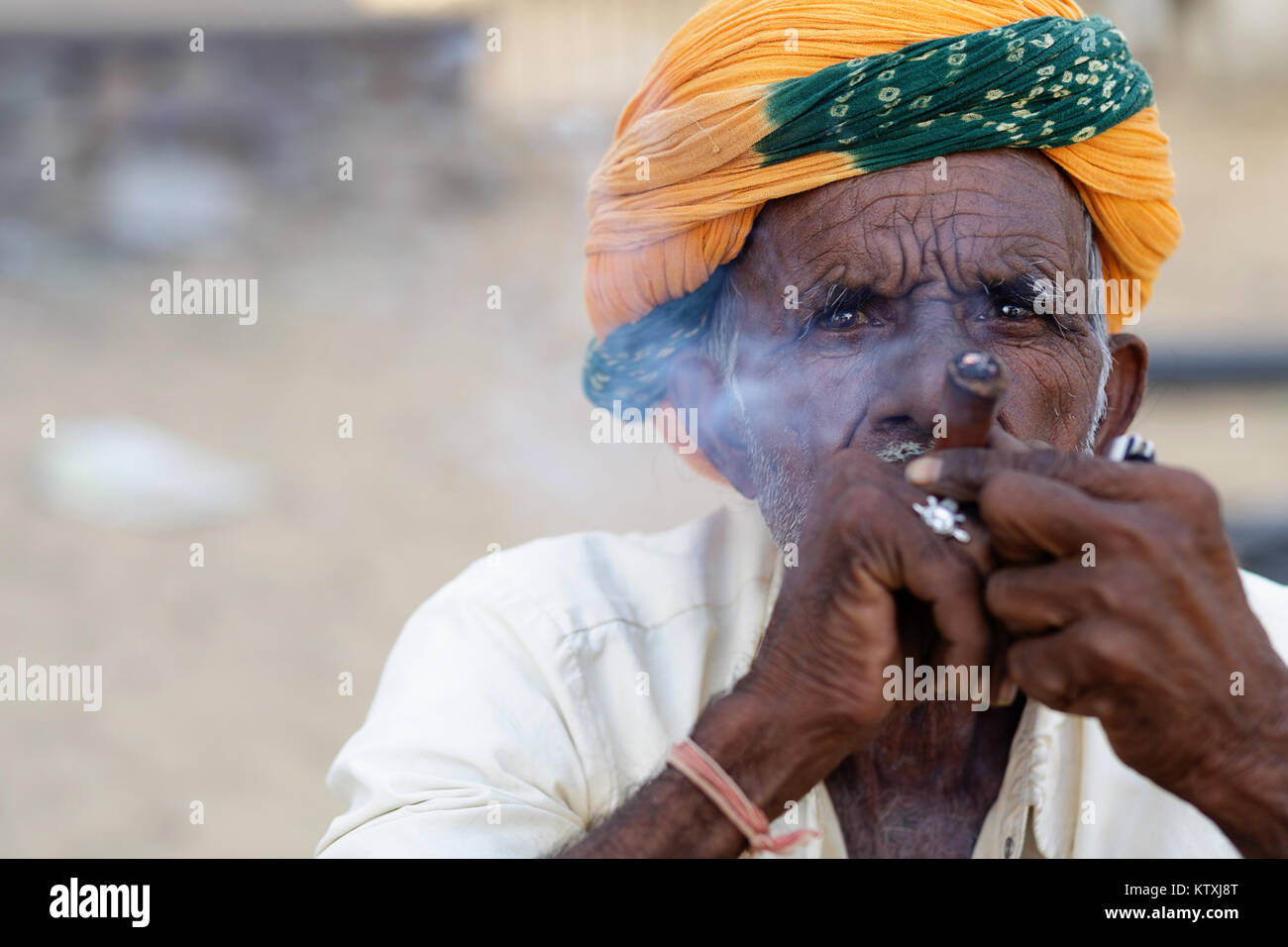 Indische Mann mit der Gelben Turbane rauchen Zigarre, ein traditionelles Dorf in der Nähe von Pushkar, Rajasthan, Indien. Stockfoto