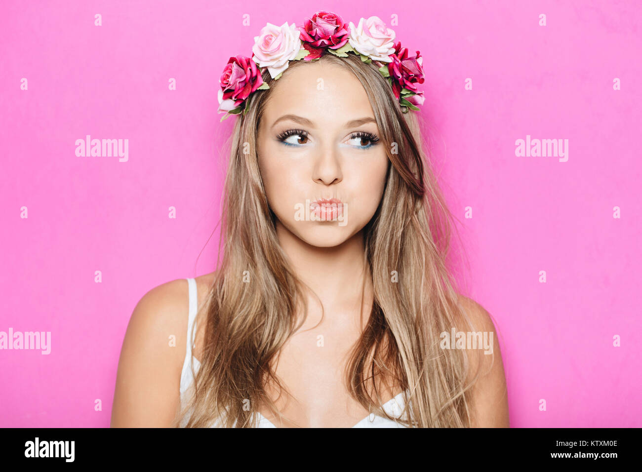 Lustig, hübsches Mädchen, Puffing ihre Wangen gegen Studio rosa Hintergrund. Headshot der charmante blonde junge Frau mit Blumen im Haar, die Münder whi Stockfoto