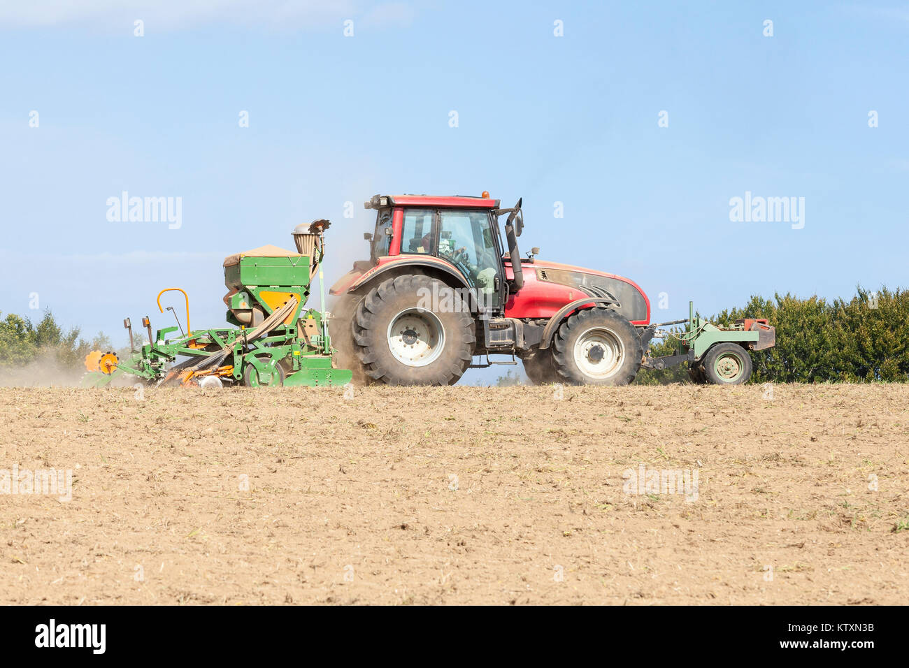 Bauer Pflanzen und Säen eine Frühling-ernte mit Traktor und Amazone Sämaschine in einem brachliegenden Feld in einer Nahaufnahme Seite Blick auf die Skyline mit Kopie spac Stockfoto
