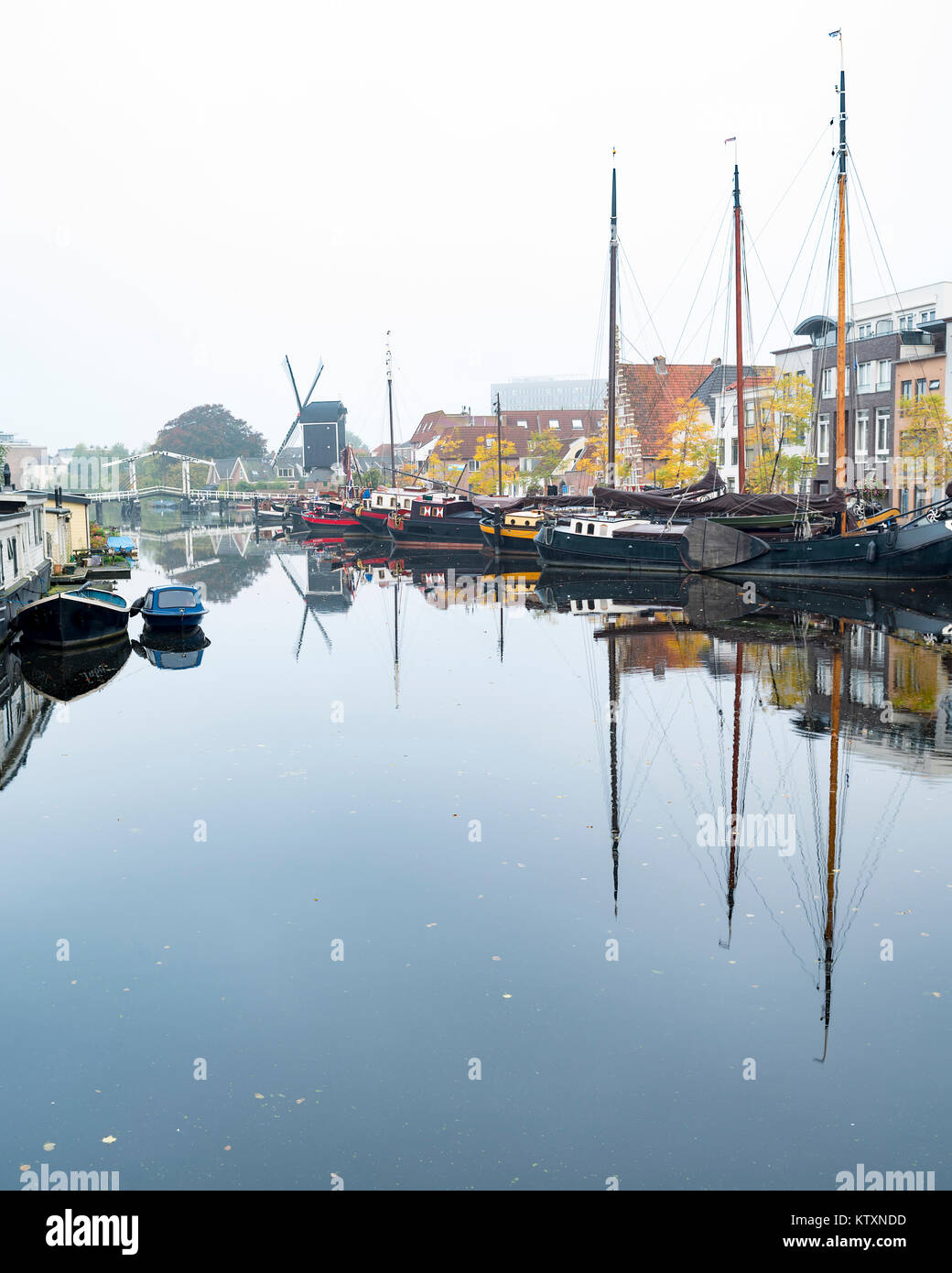 Schiffe, Windmühle und Häuser befinden sich in einem Kanal an einem nebligen Morgen in Leiden, Niederlande nieder Stockfoto