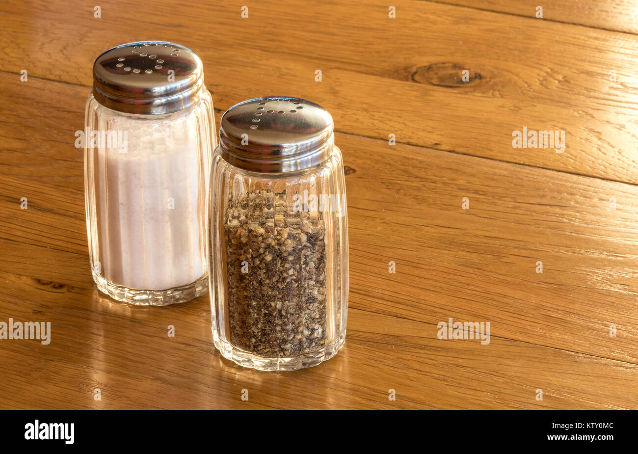 In der Nähe von Glas Salz- und Pfefferstreuer oder Salz- und Pfefferstreuer auf einem Holztisch, sehr häufig Speisen würzen auf jedem Tisch beim Essen gesehen Stockfoto