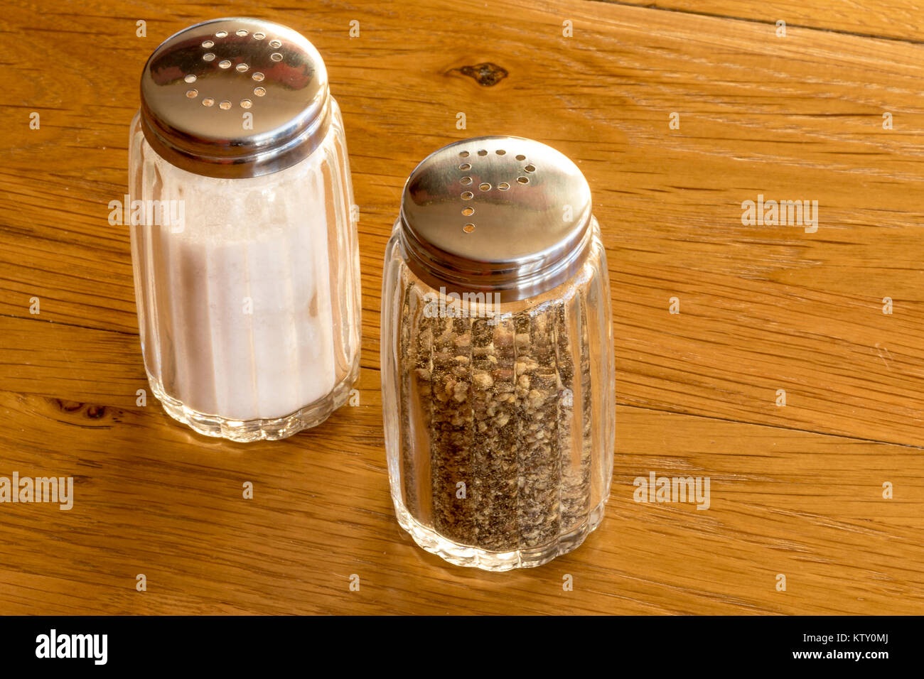 In der Nähe von Glas Salz- und Pfefferstreuer oder Salz- und Pfefferstreuer auf einem Holztisch, sehr häufig Speisen würzen auf jedem Tisch beim Essen gesehen Stockfoto