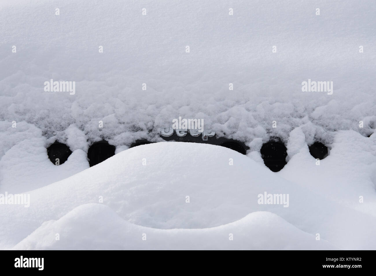 Die Front eines schwarzen Jeep Wrangler abgedeckt im Schnee mit nur der Chrom Jeep Emblem sichtbar. Stockfoto