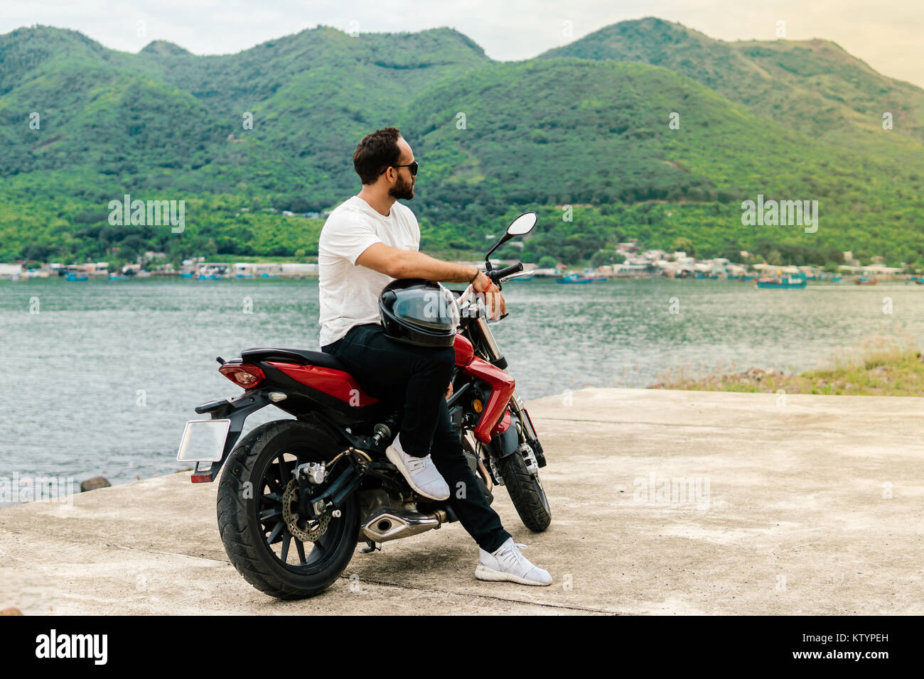 Mann sitzt auf seinem Motorrad, Helm auf Meer Hintergrund Stockfoto