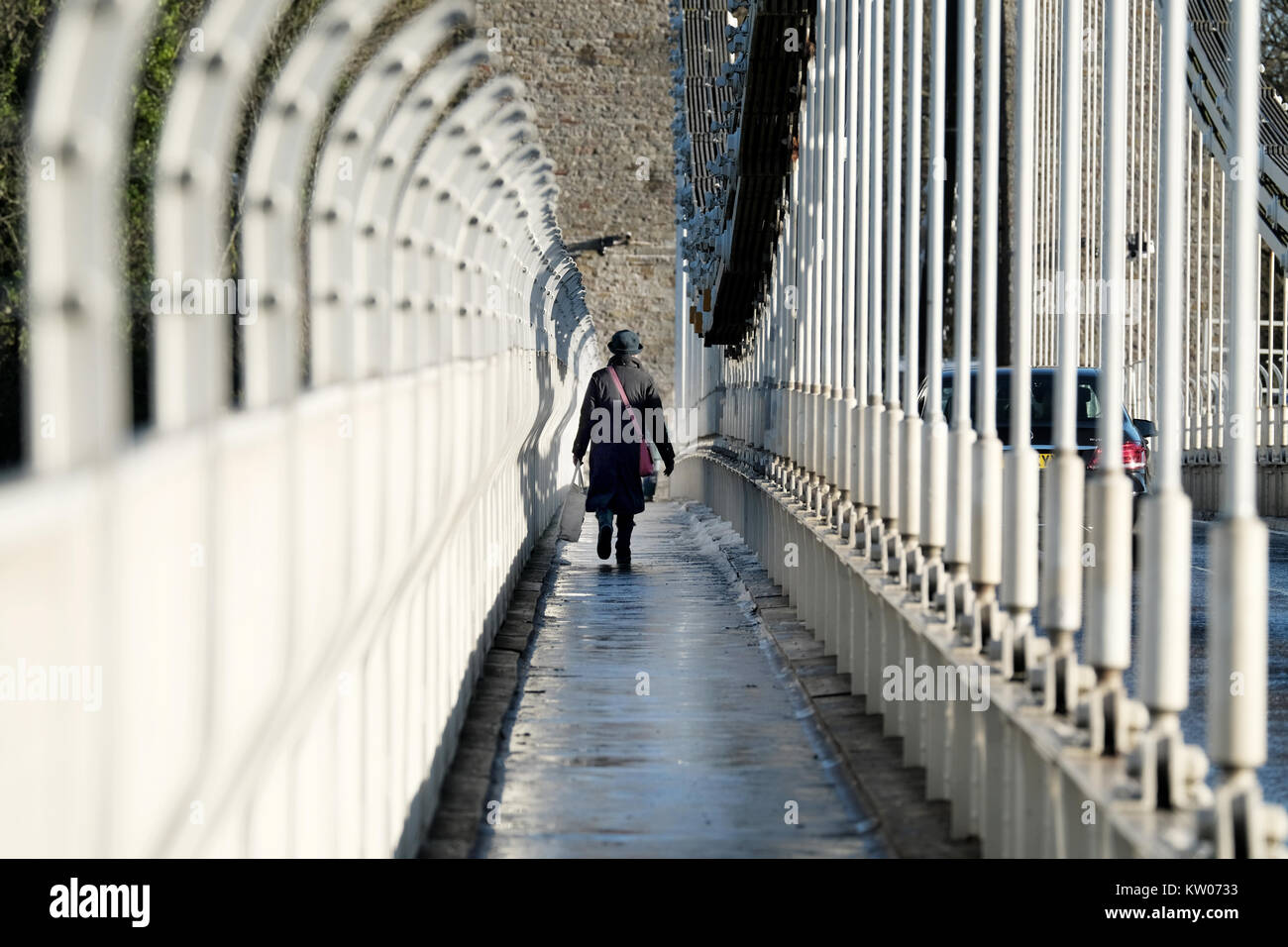 Eine Frau, die eine große Tasche, die über die Clifton Suspension Bridge in Bristol, UK. Ein kalter Wintertag und es gibt Eis und Schnee auf dem Gehweg. Stockfoto