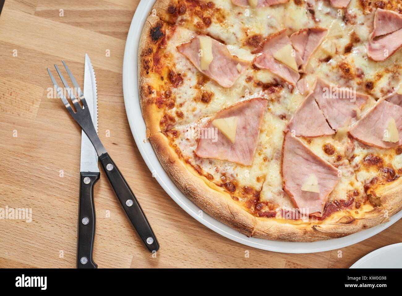 Frische Pizza mit Schinken und Ananas auf hölzernen Tisch im Restaurant. Stockfoto
