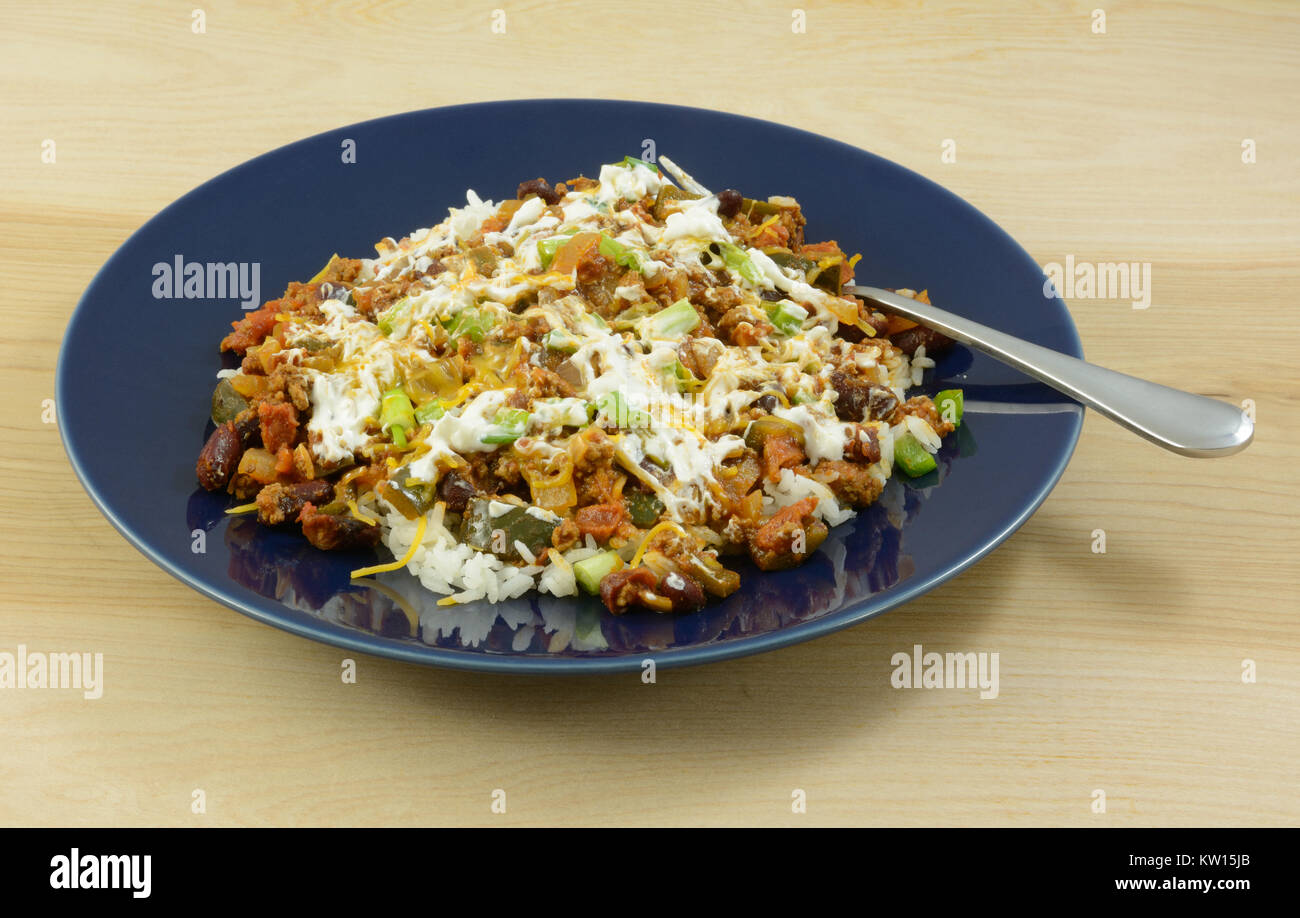 Chili auf Reis mit Sauerrahm und shredded Cheddar Käse Topping auf blaue Platte mit Gabel Stockfoto