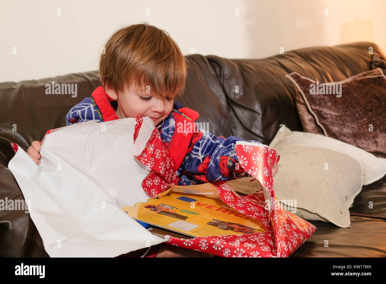 Kleinkind saß auf dem Sofa in seinem Morgenmantel ein Geschenk auf Weihnachten Morgen öffnen Stockfoto