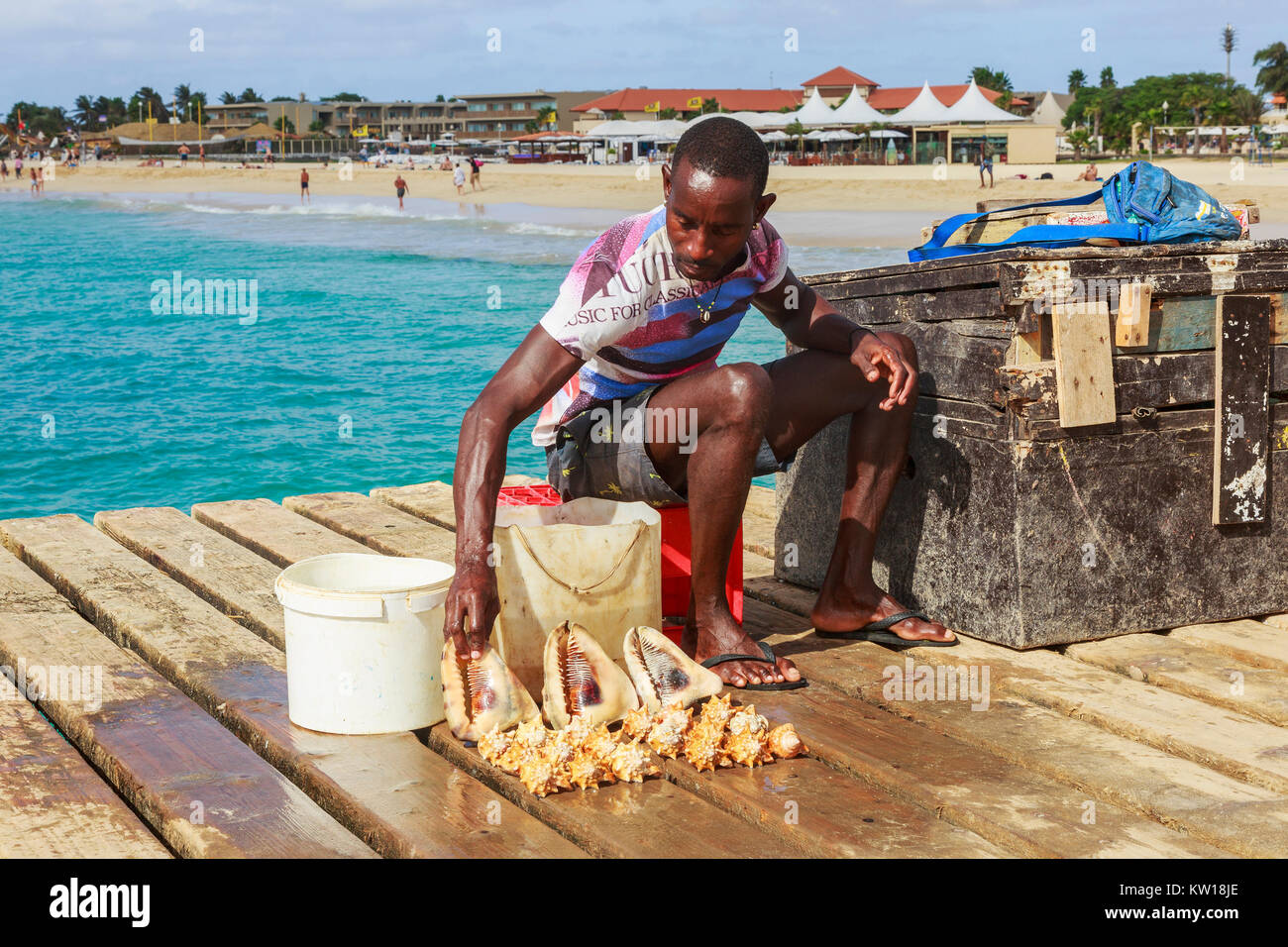 Lokaler Mann verkauf von Muscheln an Touristen auf dem hölzernen Pier in Santa Maria, Insel Sal, Salina, Kap Verde, Afrika Stockfoto