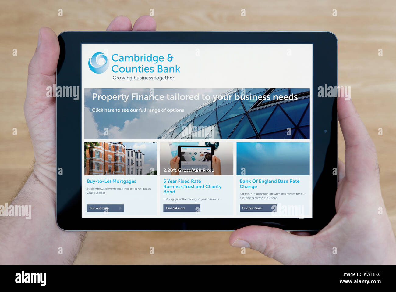 Ein Mann schaut auf die Cambridge und Grafschaften Bank Website auf seinem iPad tablet device, Schuß gegen einen hölzernen Tisch top Hintergrund (nur redaktionelle Nutzung) Stockfoto