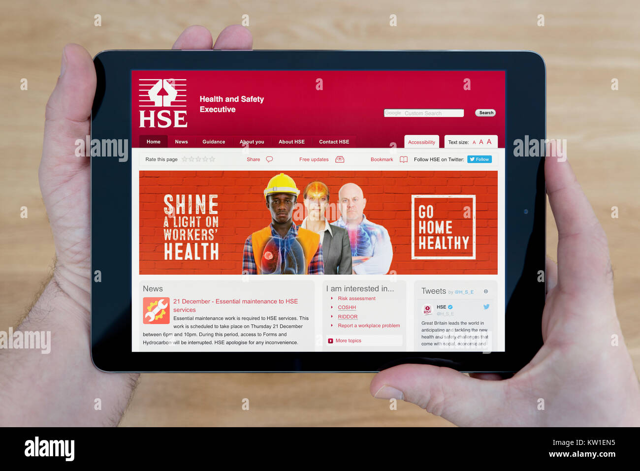 Ein Mann schaut auf die Gesundheit und Sicherheit (HSE) Website auf seinem iPad tablet device, schoß nur gegen einen hölzernen Tisch top Hintergrund - Redaktionelle Verwendung Stockfoto