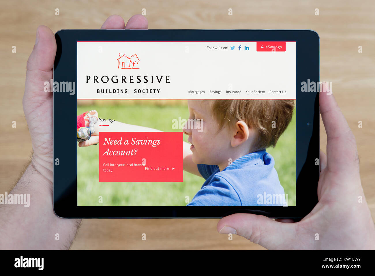 Ein Mann sieht den schrittweisen Aufbau der Gesellschaft Website auf seinem iPad tablet device, Schuß gegen einen hölzernen Tisch top Hintergrund (nur redaktionelle Nutzung) Stockfoto