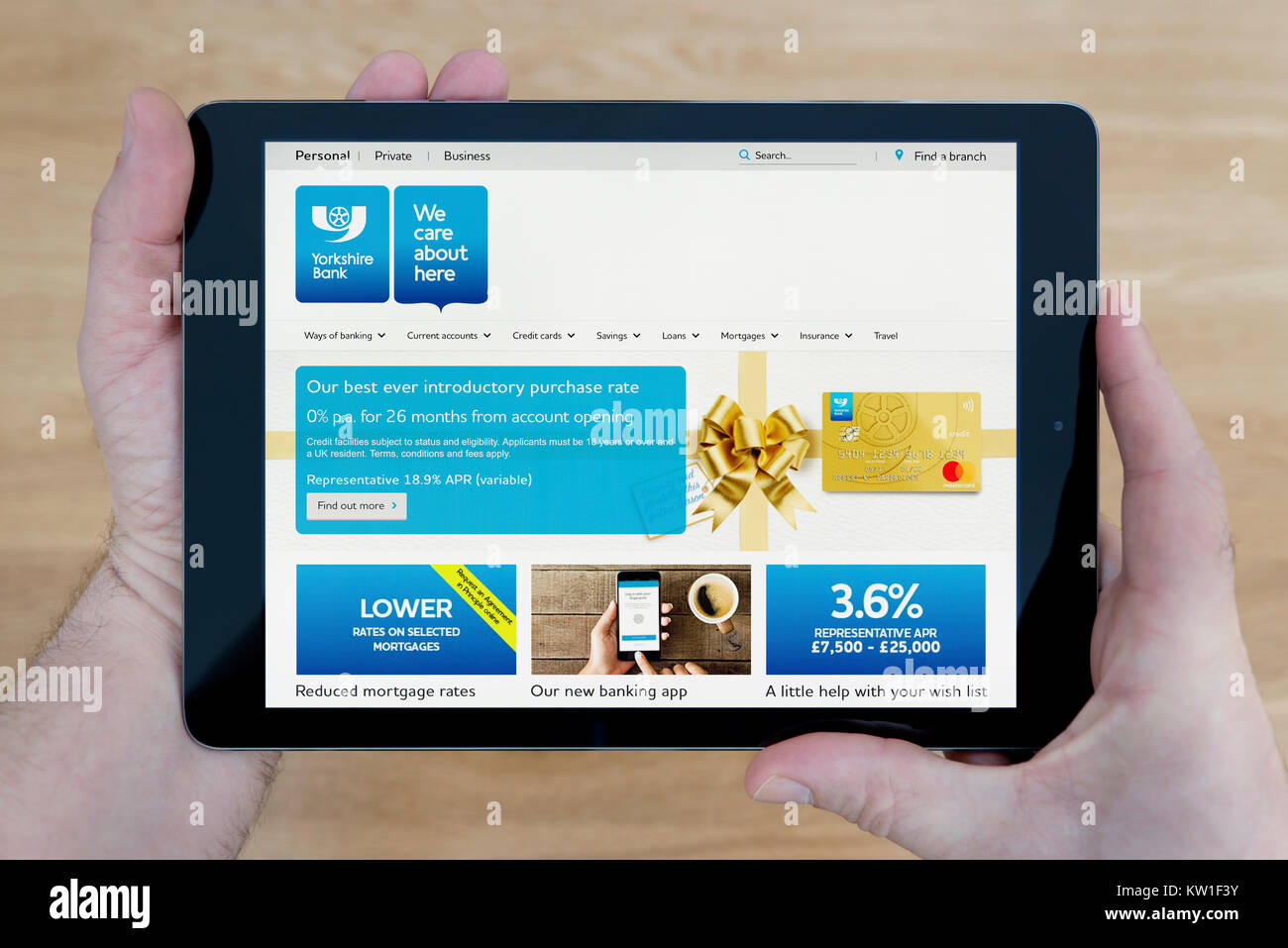 Ein Mann schaut auf die Yorkshire Bank Website auf seinem iPad tablet device, Schuß gegen einen hölzernen Tisch top Hintergrund (nur redaktionelle Nutzung) Stockfoto