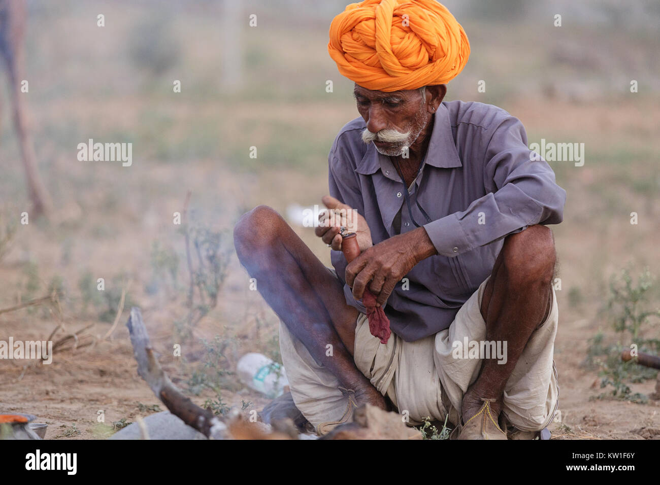 Szene in Pushkar Camel Fair, Mann in Orange turban Beleuchtung eine Zigarre am Kamin, Pushkar, Rajasthan, Indien Stockfoto
