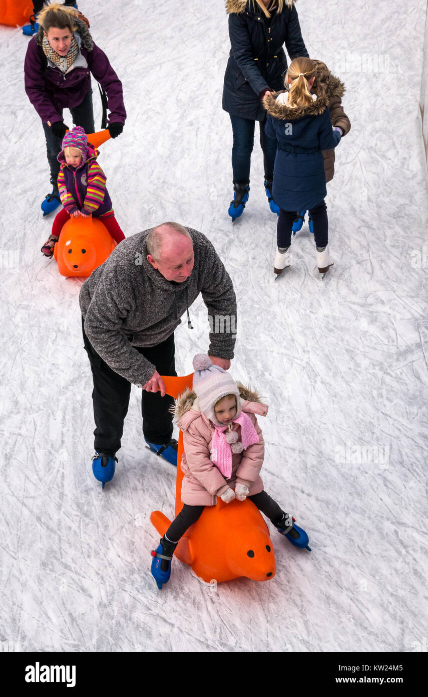 Edinburgh, Schottland, Großbritannien, 30. Dezember 2018. Familien mit kleinen Kindern genießen das Neujahrswochenende Schlittschuhlaufen auf dem St. Andrew Square. Ein Elternteil schiebt ein Kind in eine Robbeneislaufhilfe Stockfoto