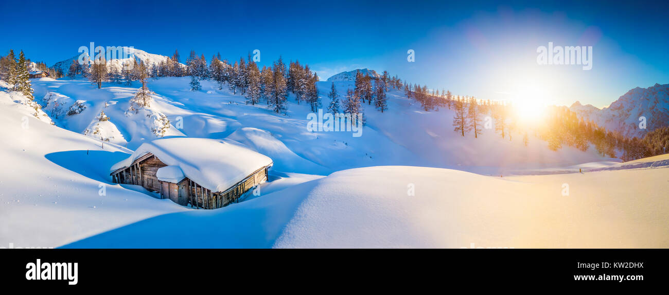 Panoramablick auf die verschneite Berglandschaft mit Schnee Berghütte in den Alpen im goldenen Abendlicht bei Sonnenuntergang mit einer Kappe bedeckt Stockfoto