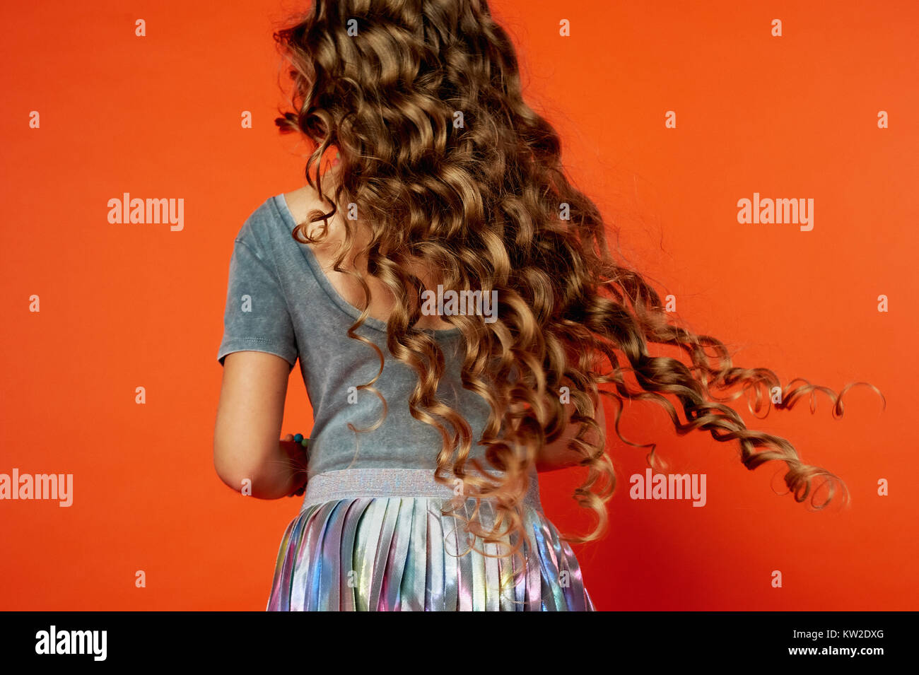 Mädchen auf orangefarbenem Hintergrund im Studio Sehr langes Mädchen auf orangefarbenem Hintergrund im Studio Sehr langes lockiges Haar wie in einem Märchen Rapunzel Entwicklung in der Bewegung