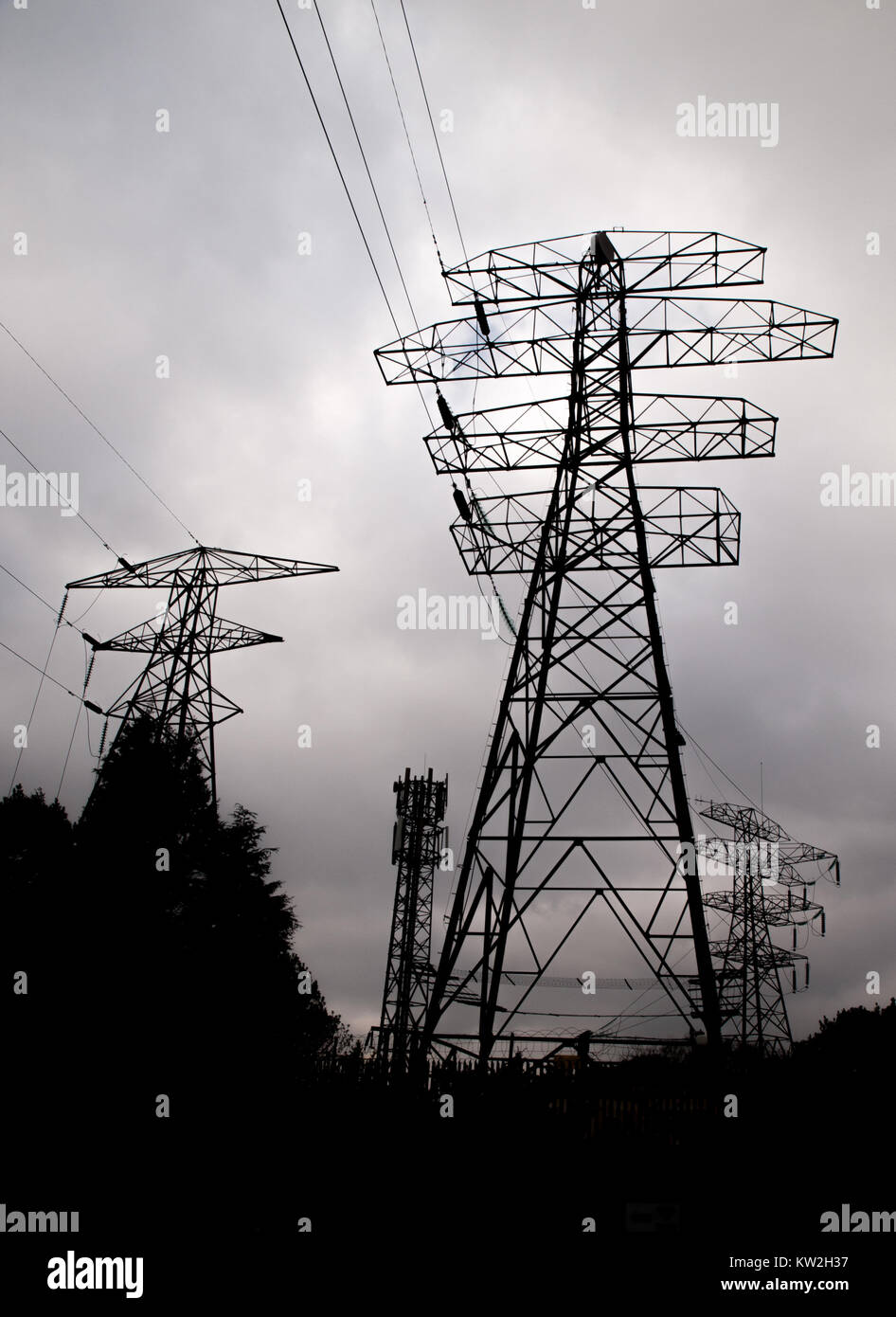 Silhouette von elecricity Pylone, Netzkabel und Handy Turm gegen einen grauen Himmel Stockfoto